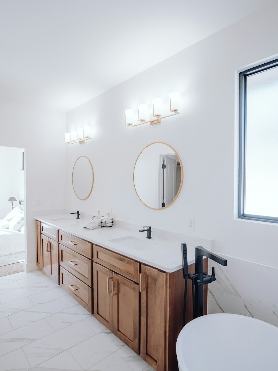 A bright bathroom with a double vanity, round mirrors and a white tub