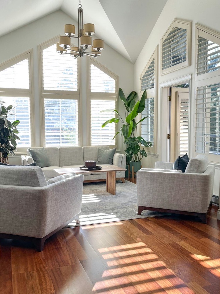A sunny living room with tall windows, wood floors and white sofas